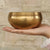 Handmade antique singing bowl with wooden mallet on red cushion, set in a forest stream for meditation and spiritual clarity.